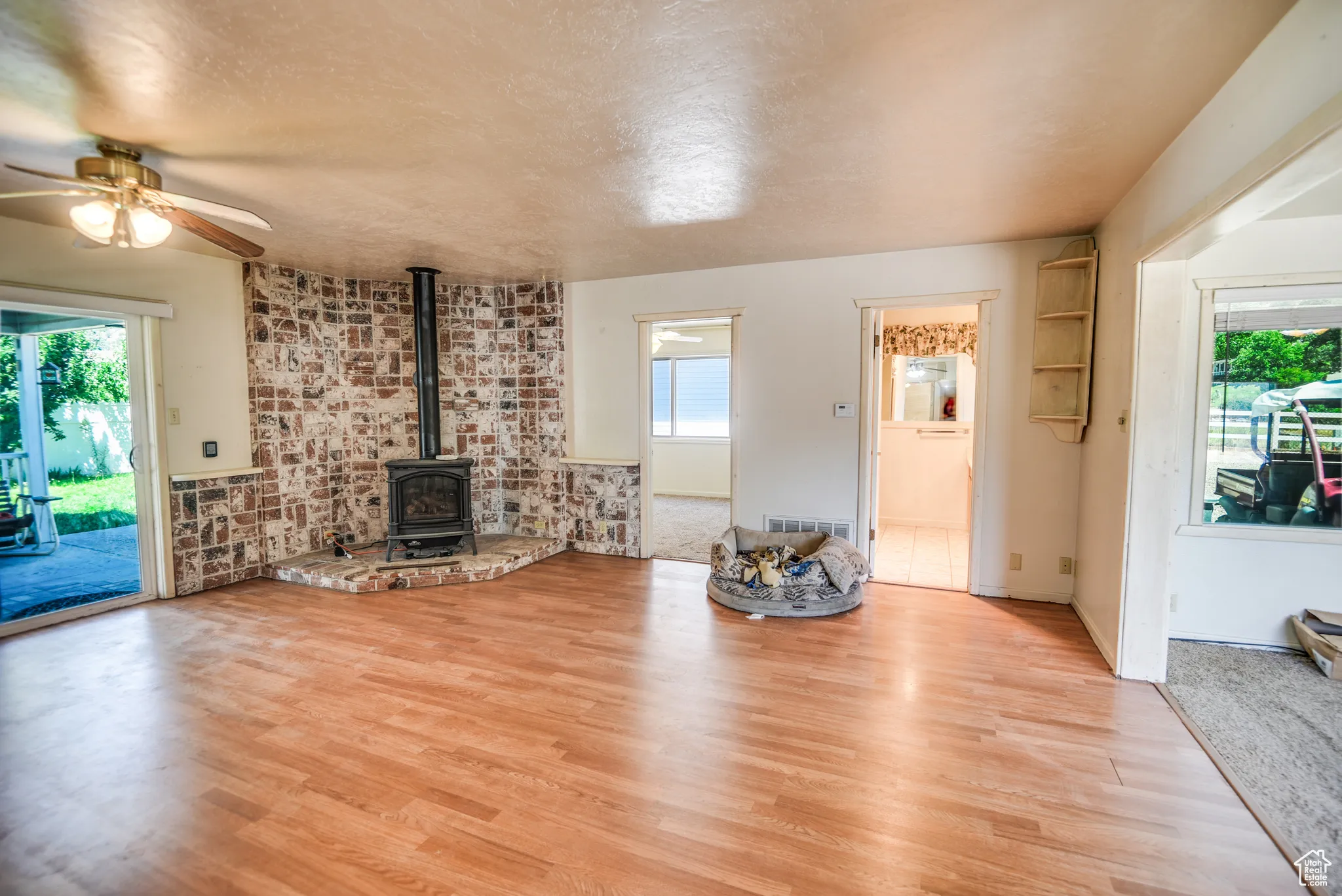 Unfurnished living room with a wood stove, light wood-style floors, ceiling fan, and a textured ceiling