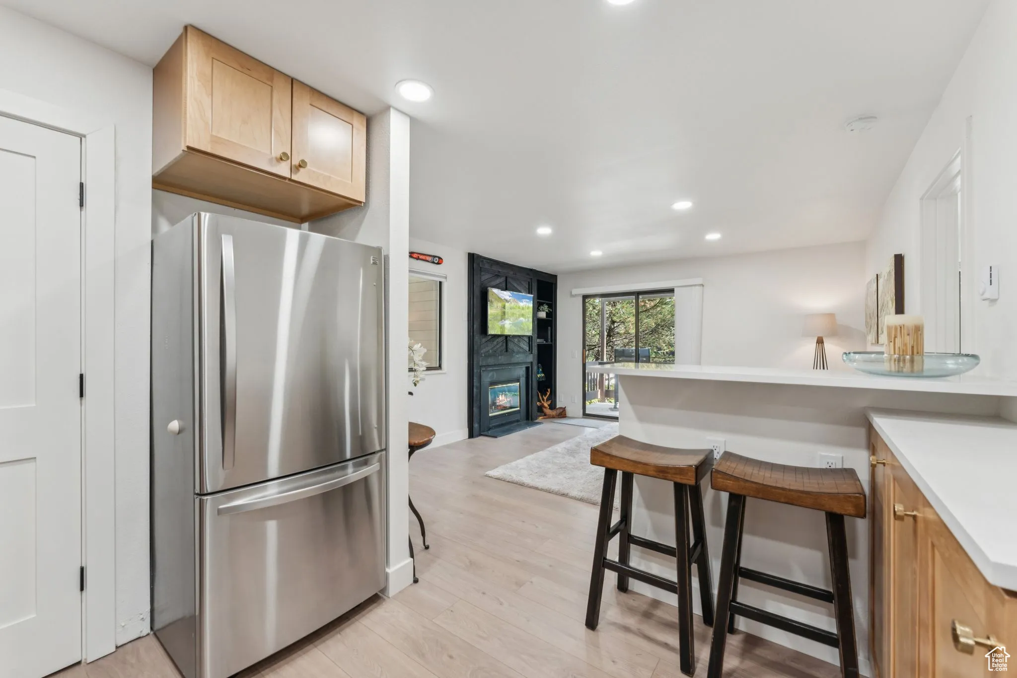 Kitchen featuring freestanding refrigerator, light countertops, light wood-type flooring, recessed lighting, and a kitchen breakfast bar