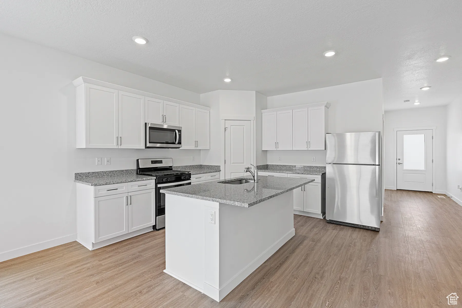 Kitchen featuring appliances with stainless steel finishes, light stone counters, white cabinets, light wood-style flooring, and a center island with sink