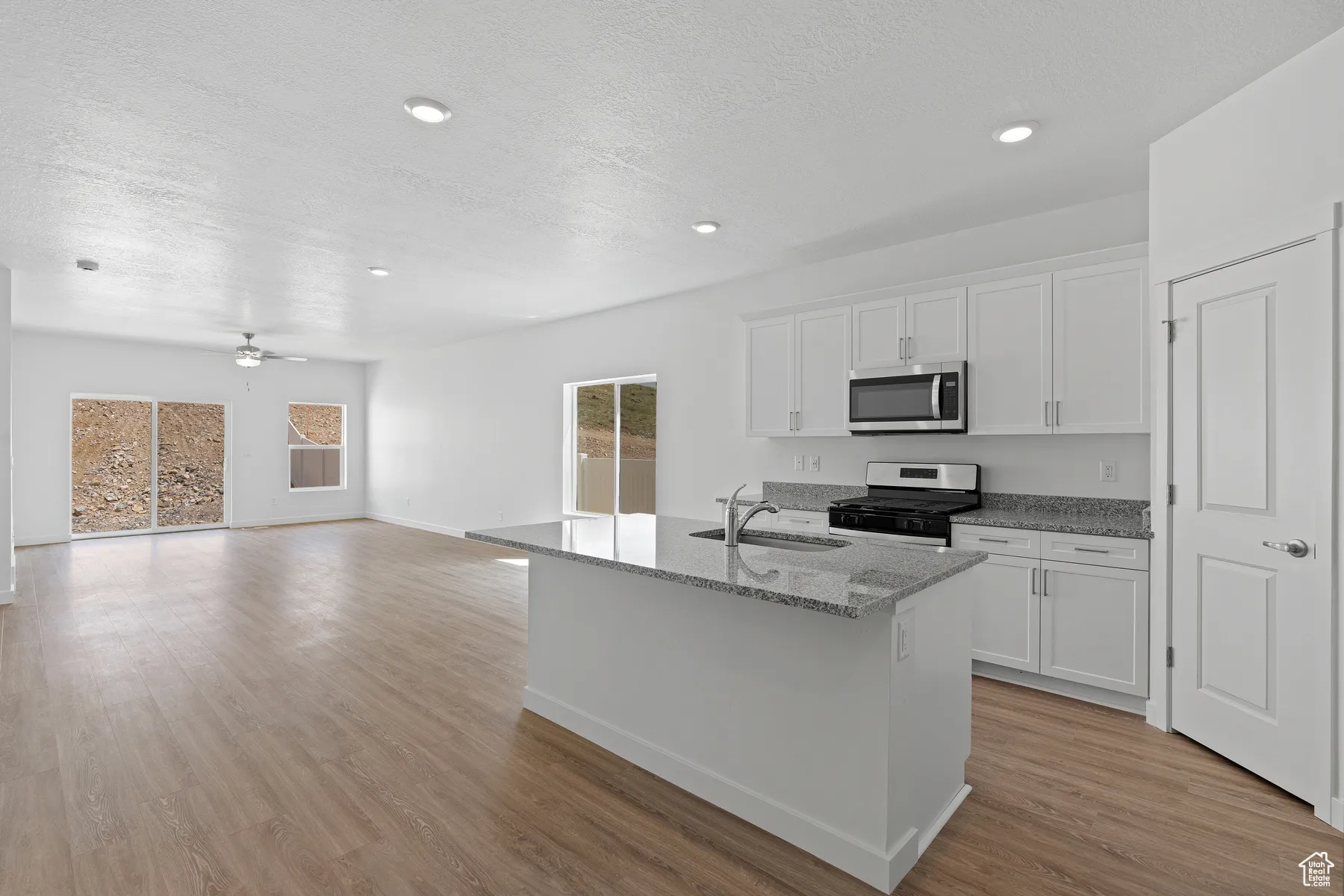 Kitchen with white cabinets, light stone countertops, gas range oven, a center island with sink, and light wood finished floors