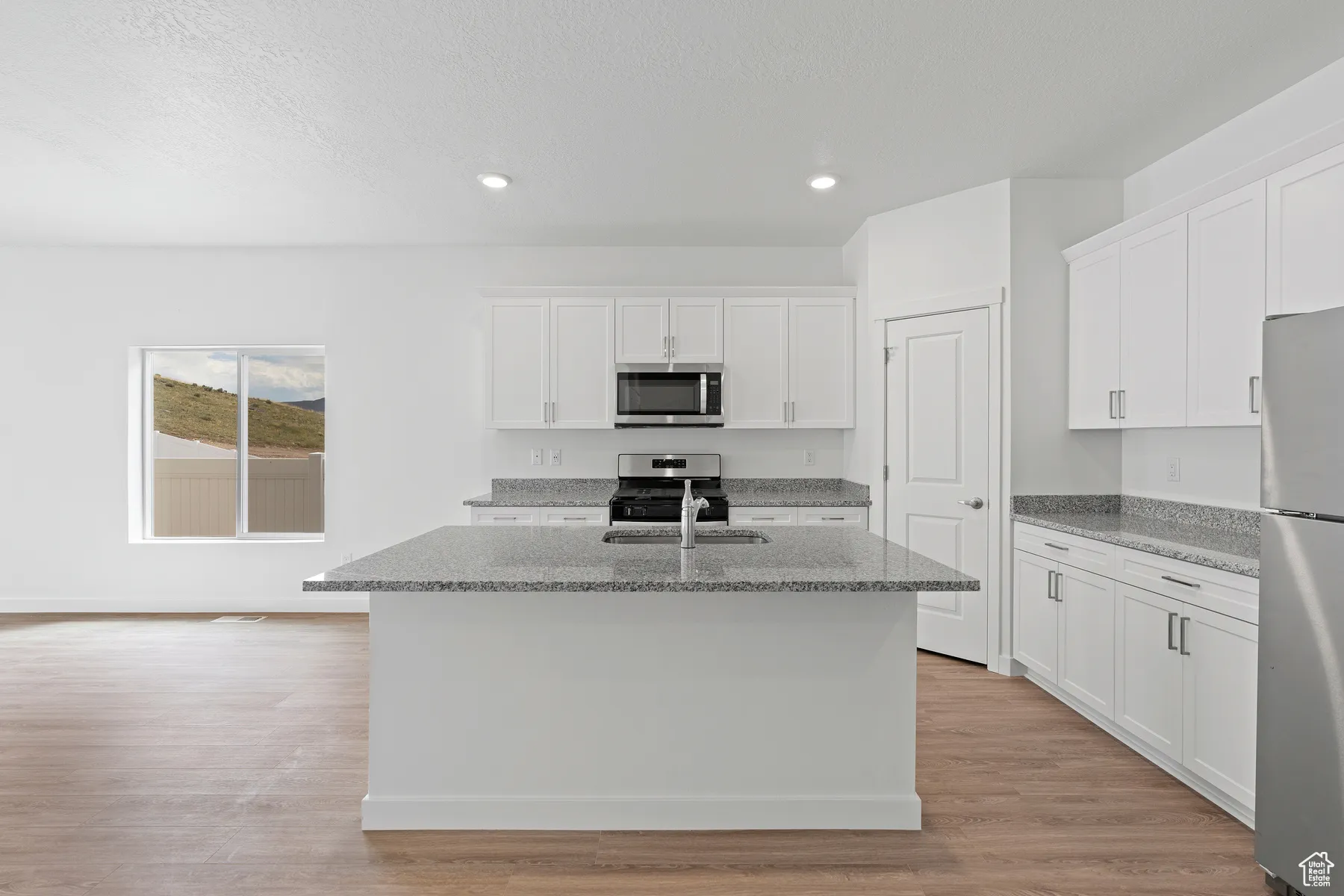 Kitchen featuring light stone counters, white cabinetry, stainless steel appliances, light wood-type flooring, and an island with sink