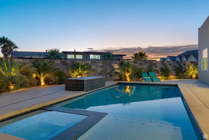 Pool at dusk with a patio, a fenced backyard, and a pool with connected hot tub. there is a water and fire feature not o in this photo.