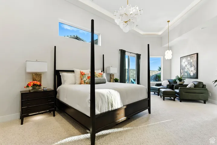 Primary bedroom with a chandelier, light colored carpet, a high tray ceiling, private seating area, stunning bath and private exterior entrance.