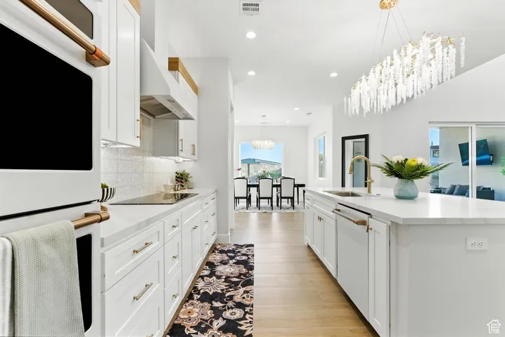 Bright kitchen featuring white appliances, tasteful backsplash, recessed lighting, an island with sink, and white cabinetry