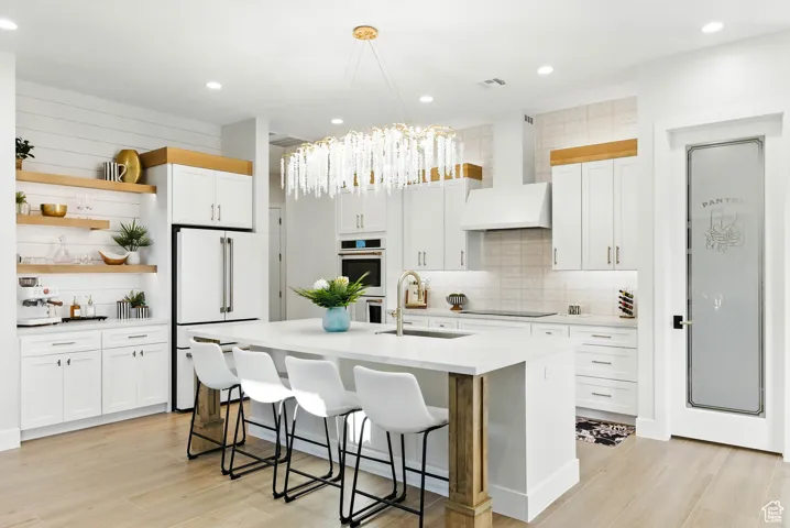 Kitchen with open shelves, both dramatic statement and lighting, white appliances, light countertops, and a breakfast bar