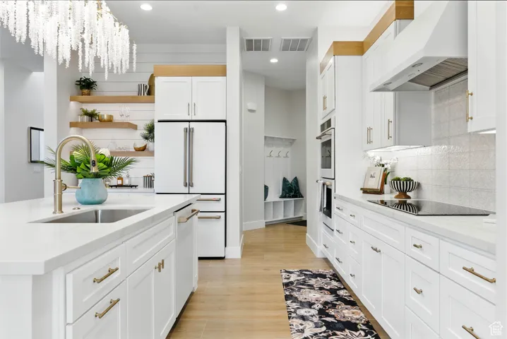 Bright white kitchen featuring open shelves, under cabinet range hood, white appliances, tile backsplash, and white cabinets