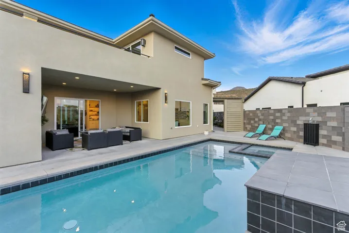 View of pool with a patio area, an outdoor living space, and a pool with connected hot tub. There is an outdoor shower tucked around the corner.