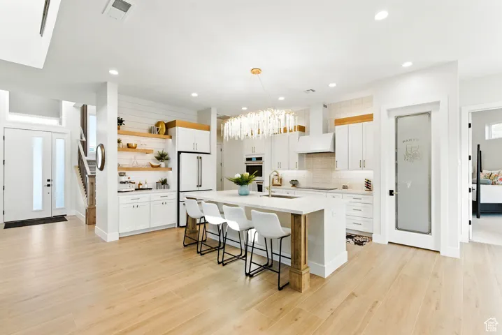 Kitchen featuring open shelves, a kitchen bar, decorative backsplash, an island with sink, and light countertops