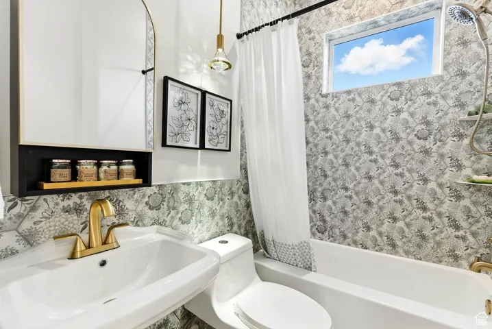 Beautiful full bath featuring shower / bath combination with curtain and wallpapered walls. Did you notice the diamond drop lighting pendant?