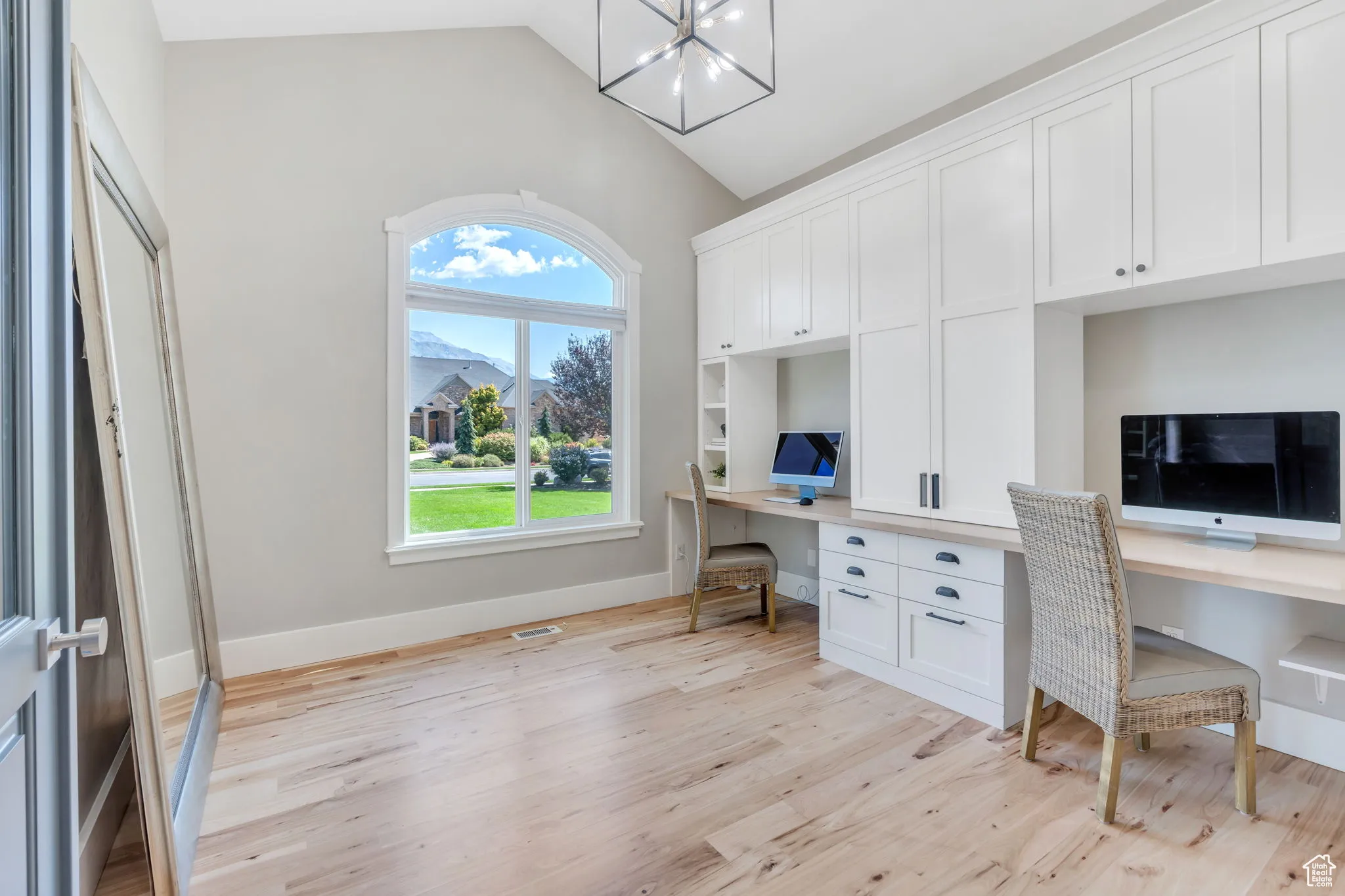Office area featuring built in desk, lofted ceiling, light wood-style floors, and a chandelier