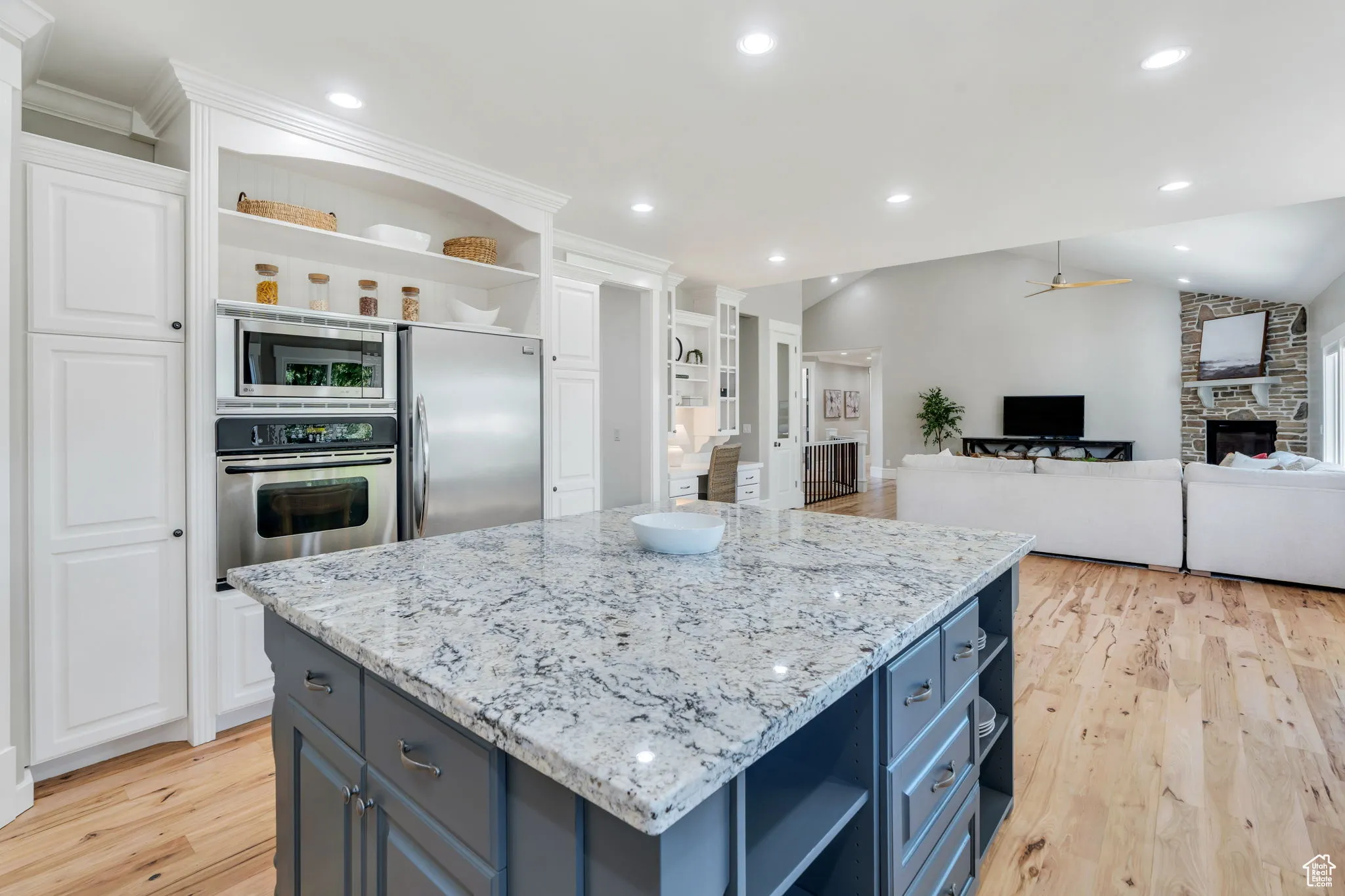 Kitchen with open shelves, a stone fireplace, vaulted ceiling, light wood-type flooring, and recessed lighting