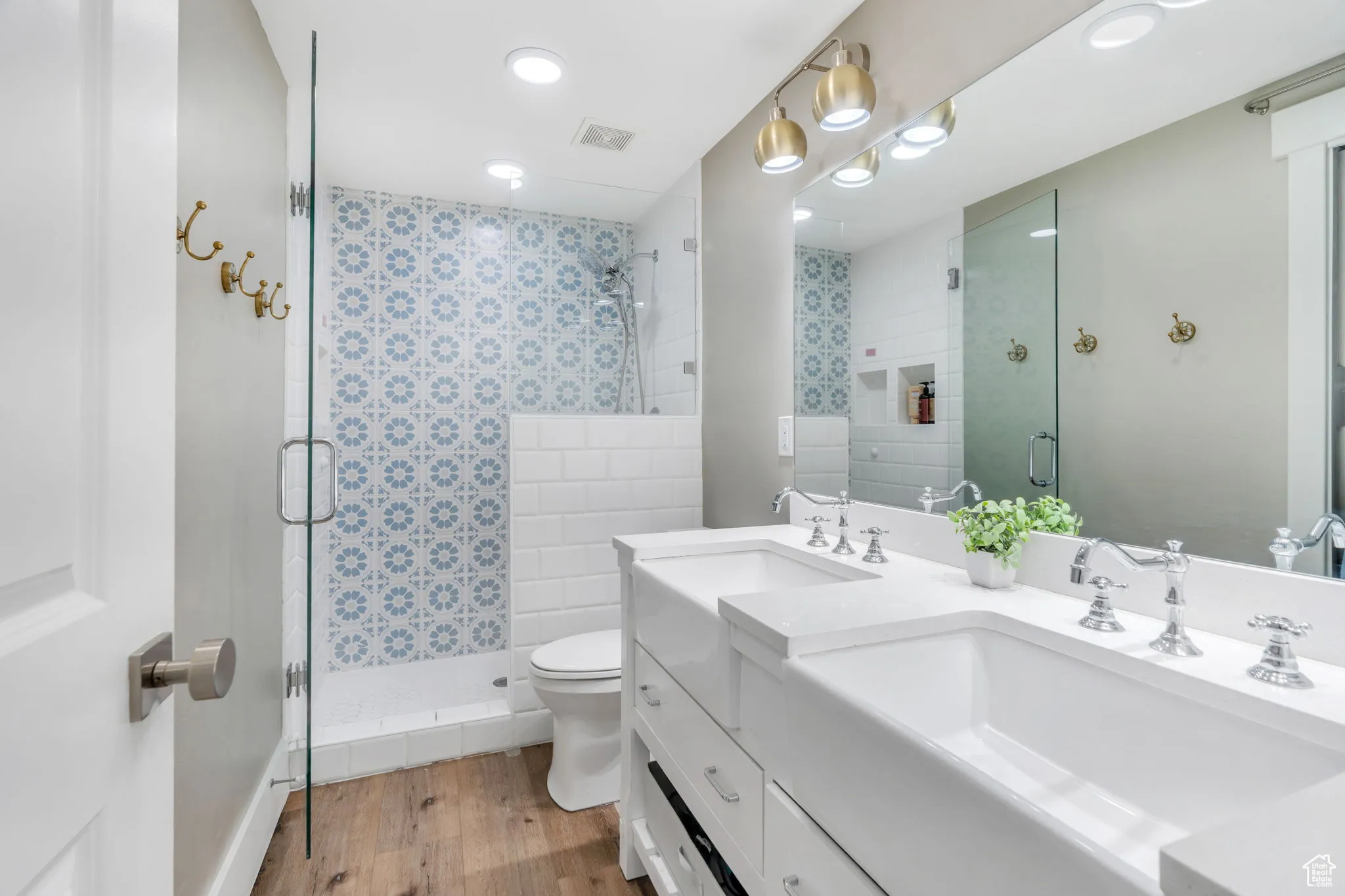 Bathroom with light wood-style floors, a shower stall, and double vanity