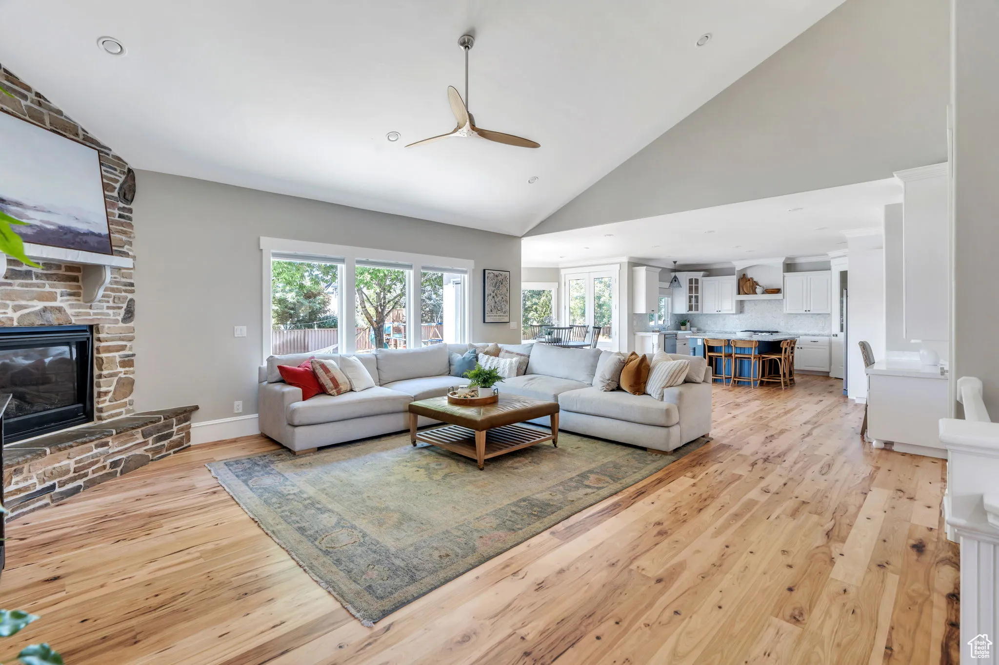 Living area with high vaulted ceiling, light wood-type flooring, a ceiling fan, a fireplace, and recessed lighting