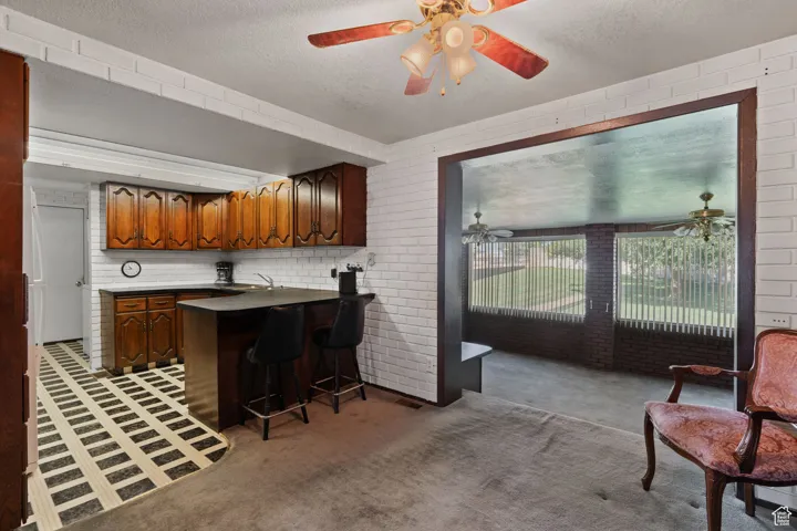Kitchen featuring a peninsula, a breakfast bar, brick wall, light carpet, and a textured ceiling
