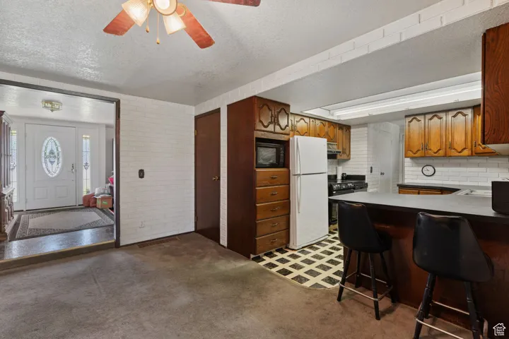 Kitchen featuring freestanding refrigerator, a textured ceiling, light colored carpet, a breakfast bar area, and black microwave
