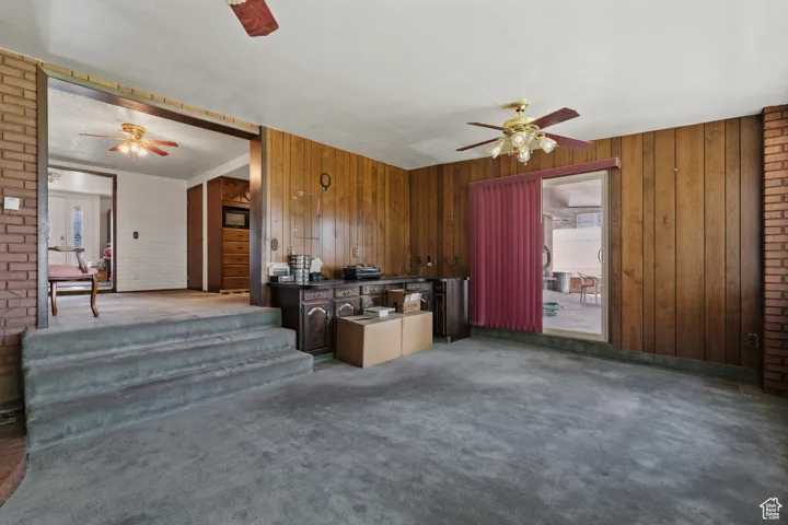 Kitchen featuring dark countertops, carpet floors, ceiling fan, brick wall, and wooden walls