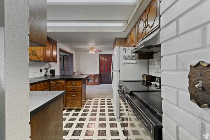 Kitchen with light floors, dark countertops, brown cabinets, and under cabinet range hood