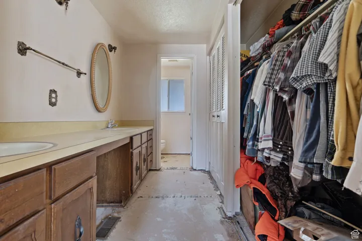 Full bathroom featuring double vanity, concrete floors, a textured ceiling, and a spacious closet