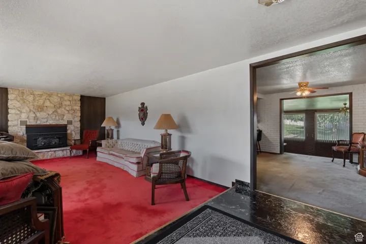 Living area with carpet floors, a textured ceiling, a stone fireplace, brick wall, and a ceiling fan