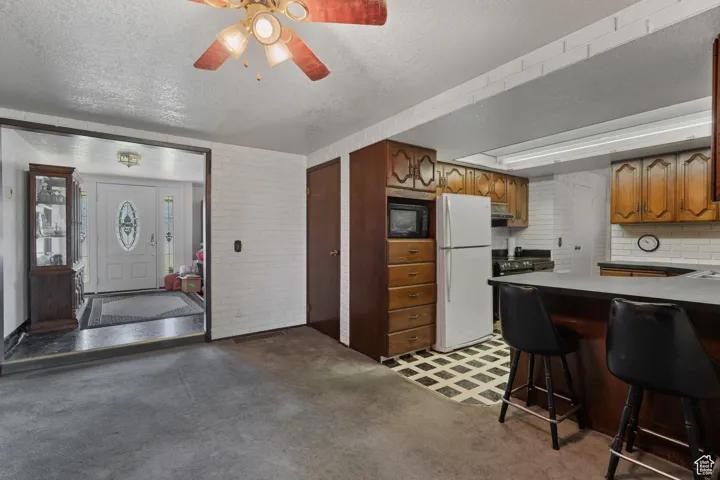 Kitchen with a textured ceiling, freestanding refrigerator, a breakfast bar area, brown cabinetry, and black microwave