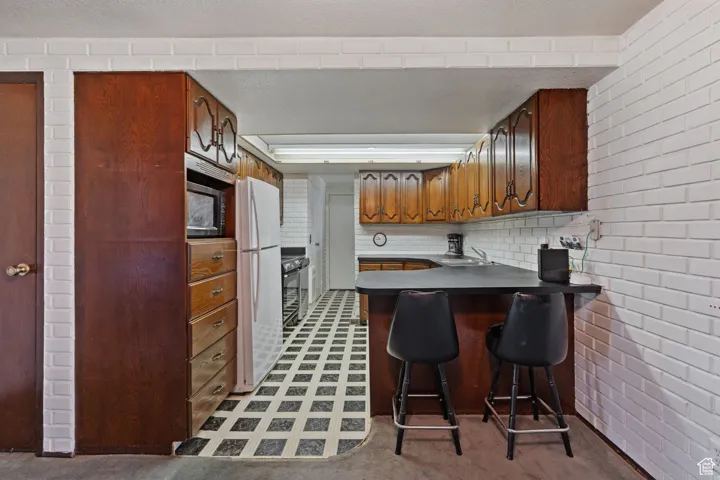 Kitchen with a breakfast bar area, a peninsula, freestanding refrigerator, dark countertops, and light floors