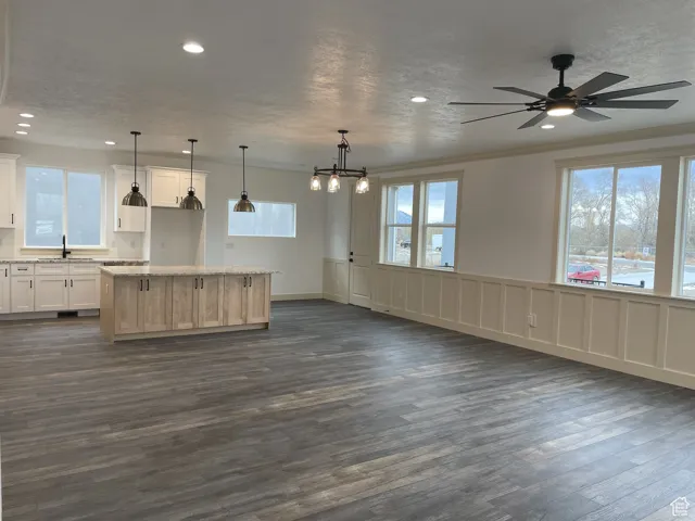 Kitchen featuring open floor plan, a center island, pendant lighting, ornamental molding, and a decorative wall