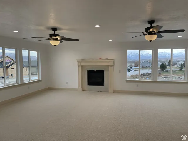 Unfurnished living room featuring a ceiling fan, a mountain view, light carpet, and recessed lighting