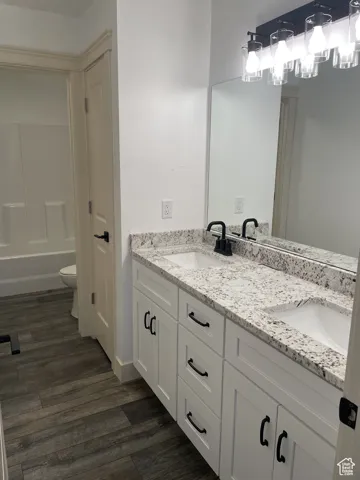 Full bathroom with double vanity, dark wood-type flooring, and shower / bath combination