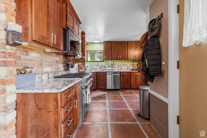 Kitchen with brown cabinets, appliances with stainless steel finishes, decorative backsplash, and light stone counters