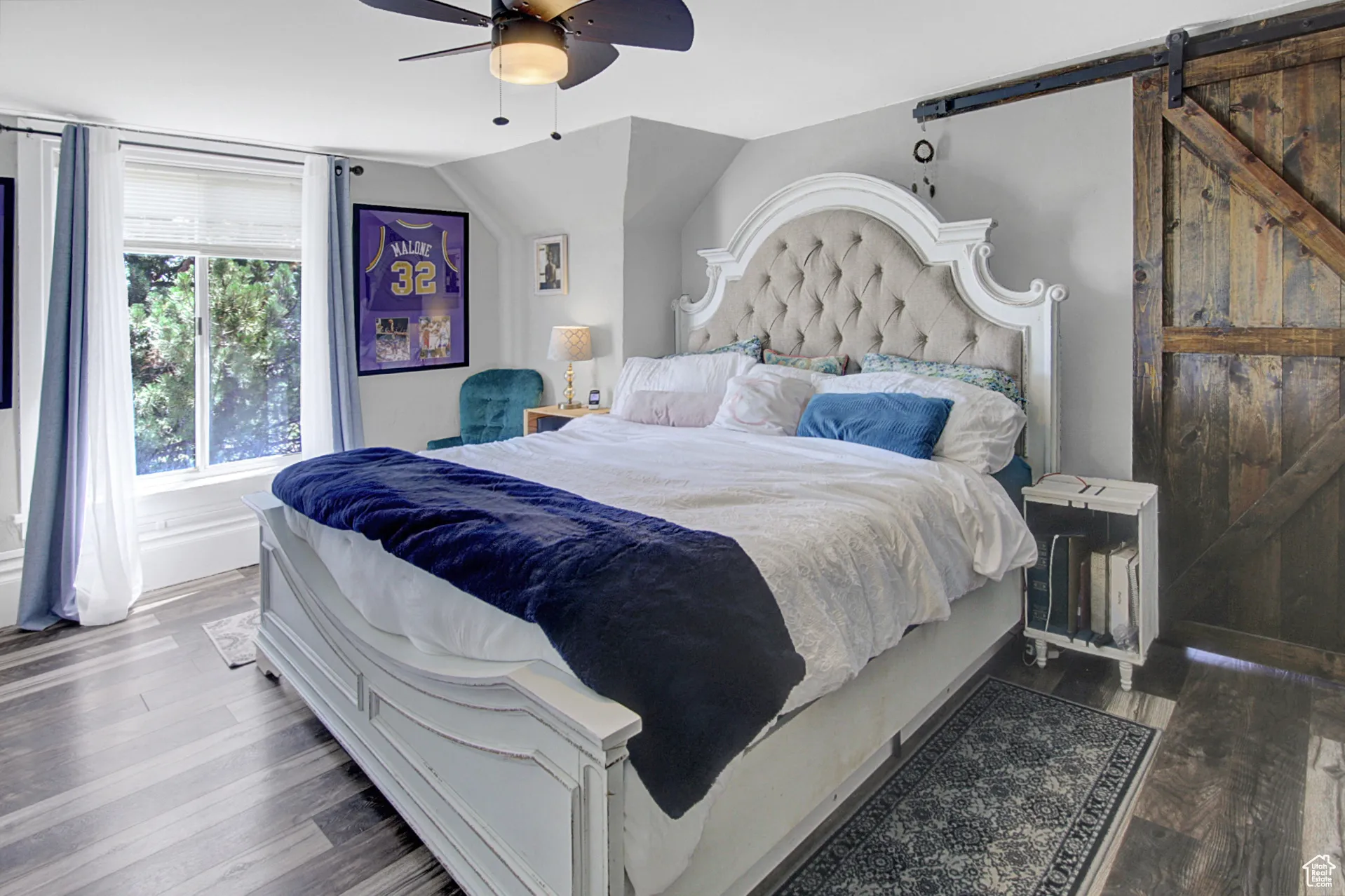 Bedroom with a barn door, wood finished floors, a ceiling fan, and vaulted ceiling