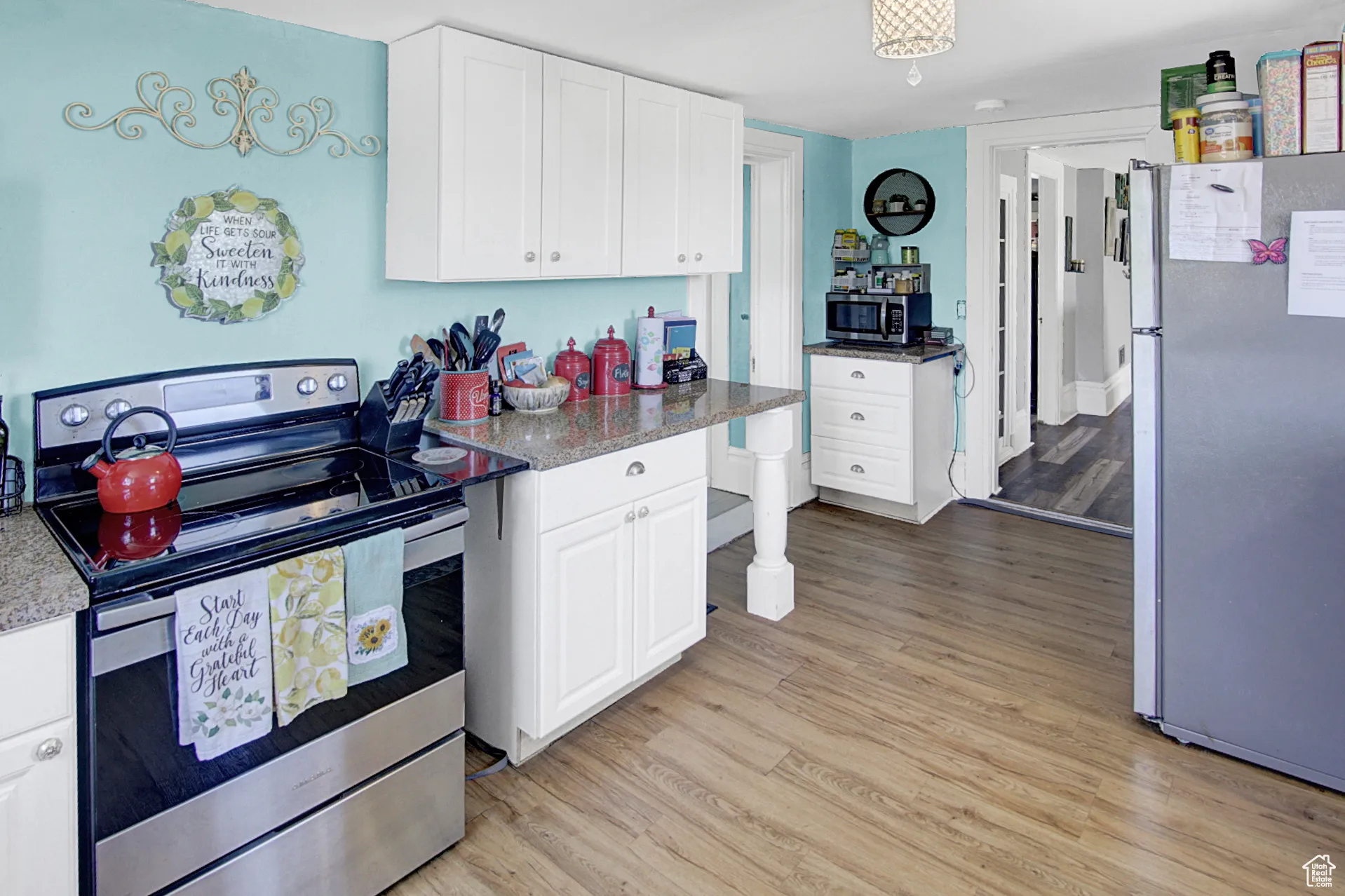 Kitchen with stainless steel appliances, white cabinetry, light wood finished floors, and light stone counters