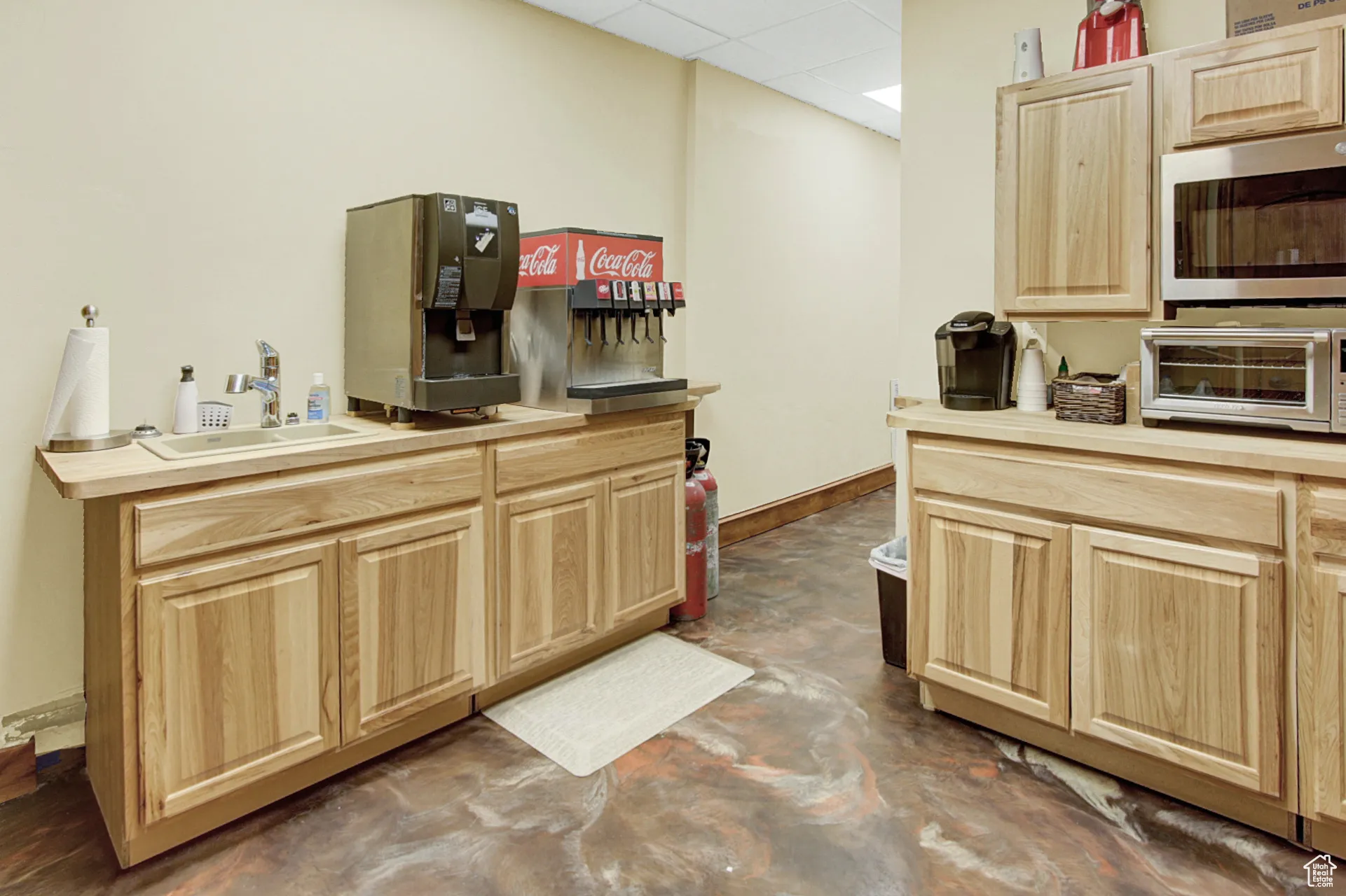 Kitchen featuring light brown cabinets, a drop ceiling, and stainless steel microwave