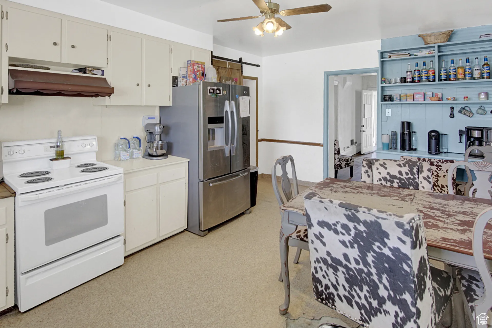 Kitchen with white electric range oven, a barn door, extractor fan, light countertops, and stainless steel refrigerator with ice dispenser