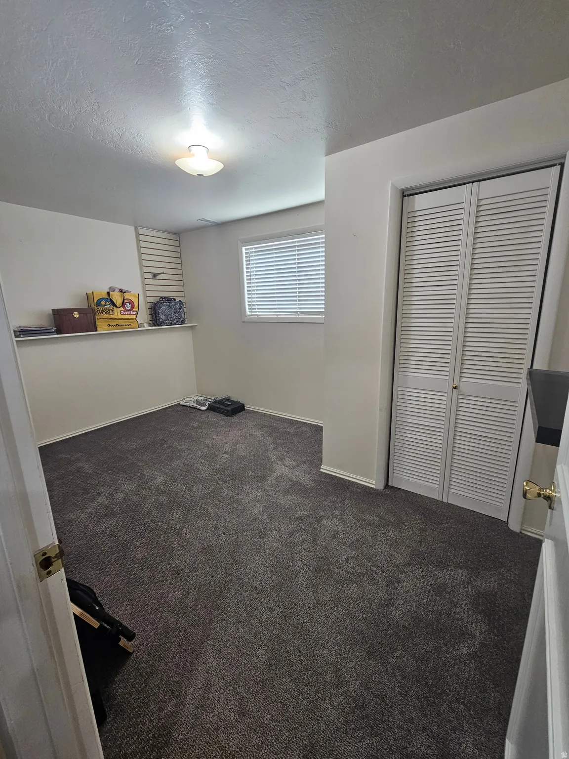 Unfurnished bedroom with a textured ceiling, dark colored carpet, and a closet