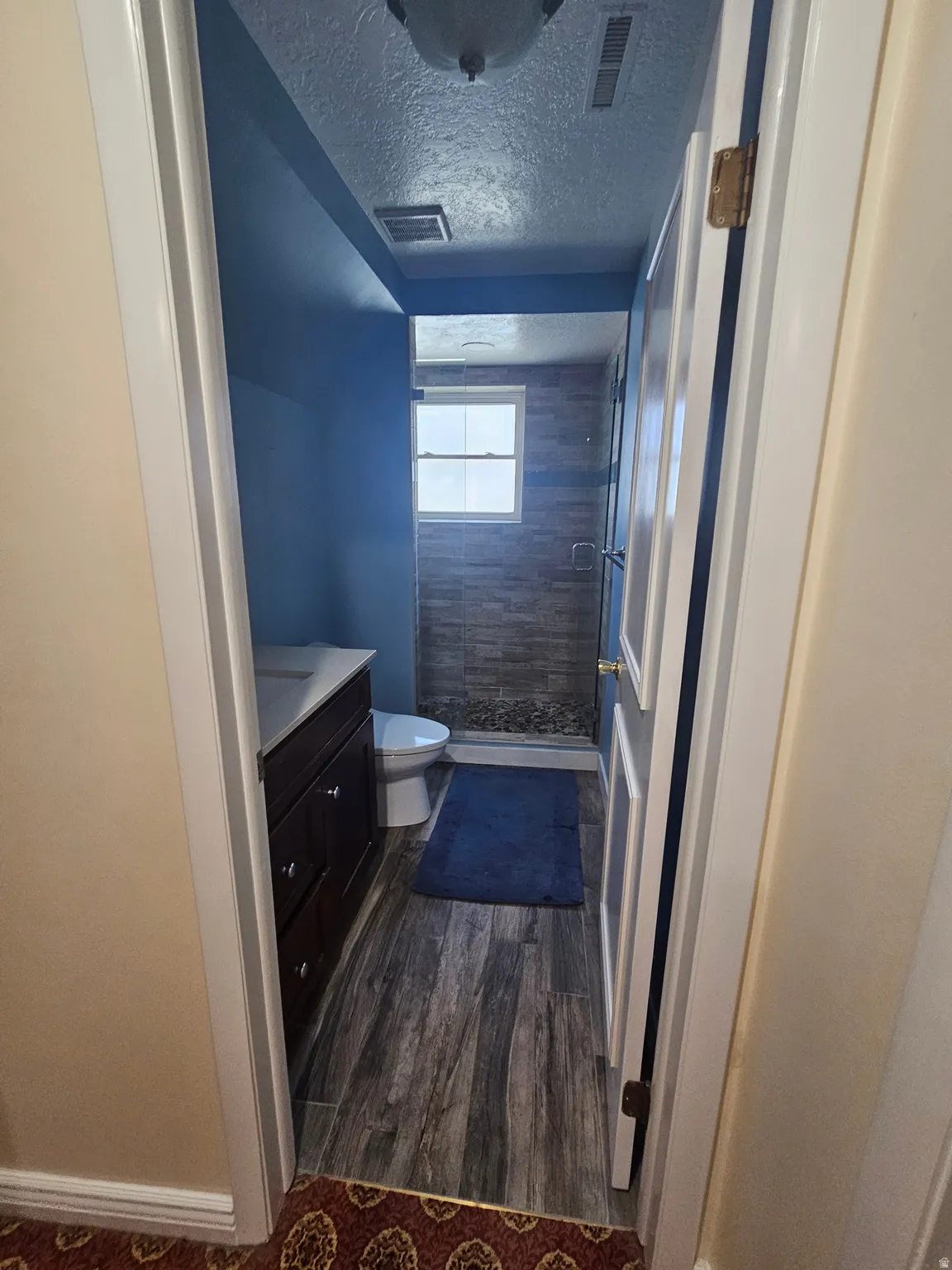 Full bathroom with a textured ceiling, a shower stall, vanity, and dark wood finished floors