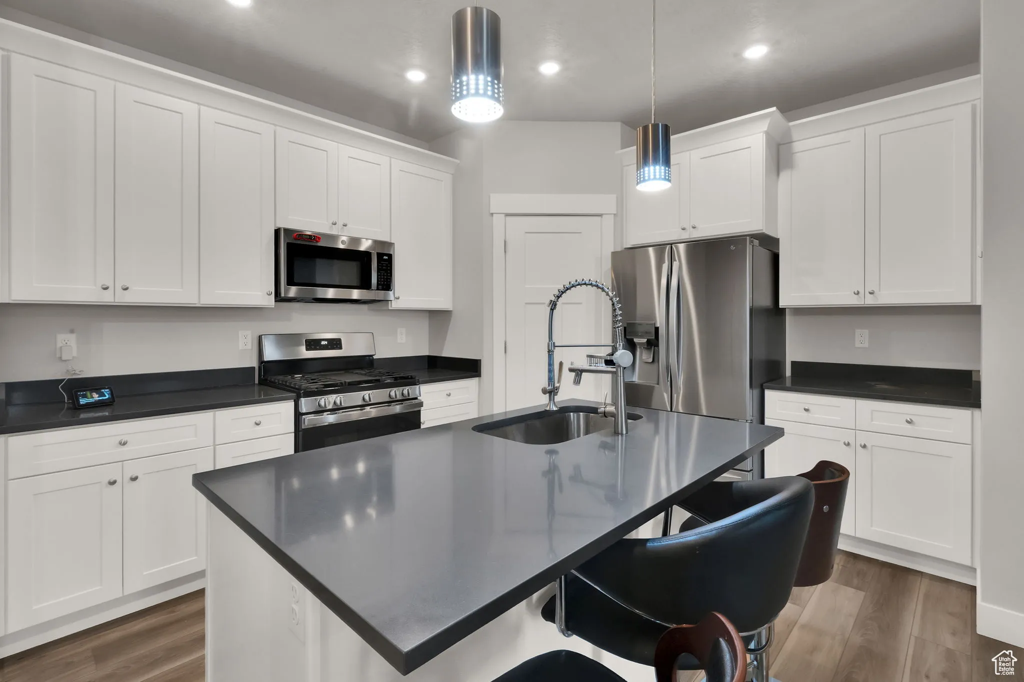 Kitchen featuring a breakfast bar, stainless steel appliances, a center island with sink, LVP wood-style floors, and upgraded pendant lighting