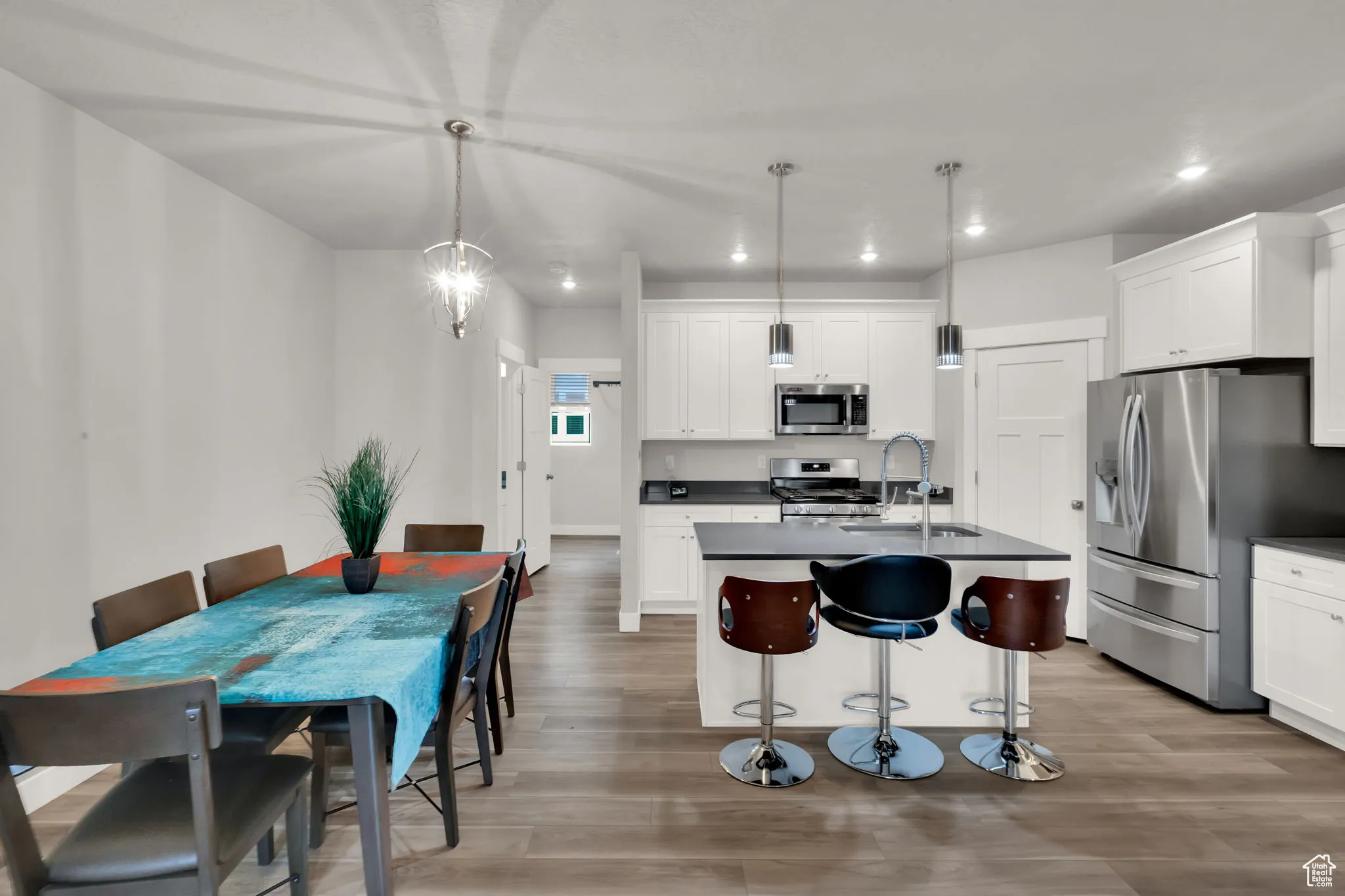 Kitchen featuring granite countertops, a kitchen bar, stainless steel appliances, custom pendant lighting, and white cabinets