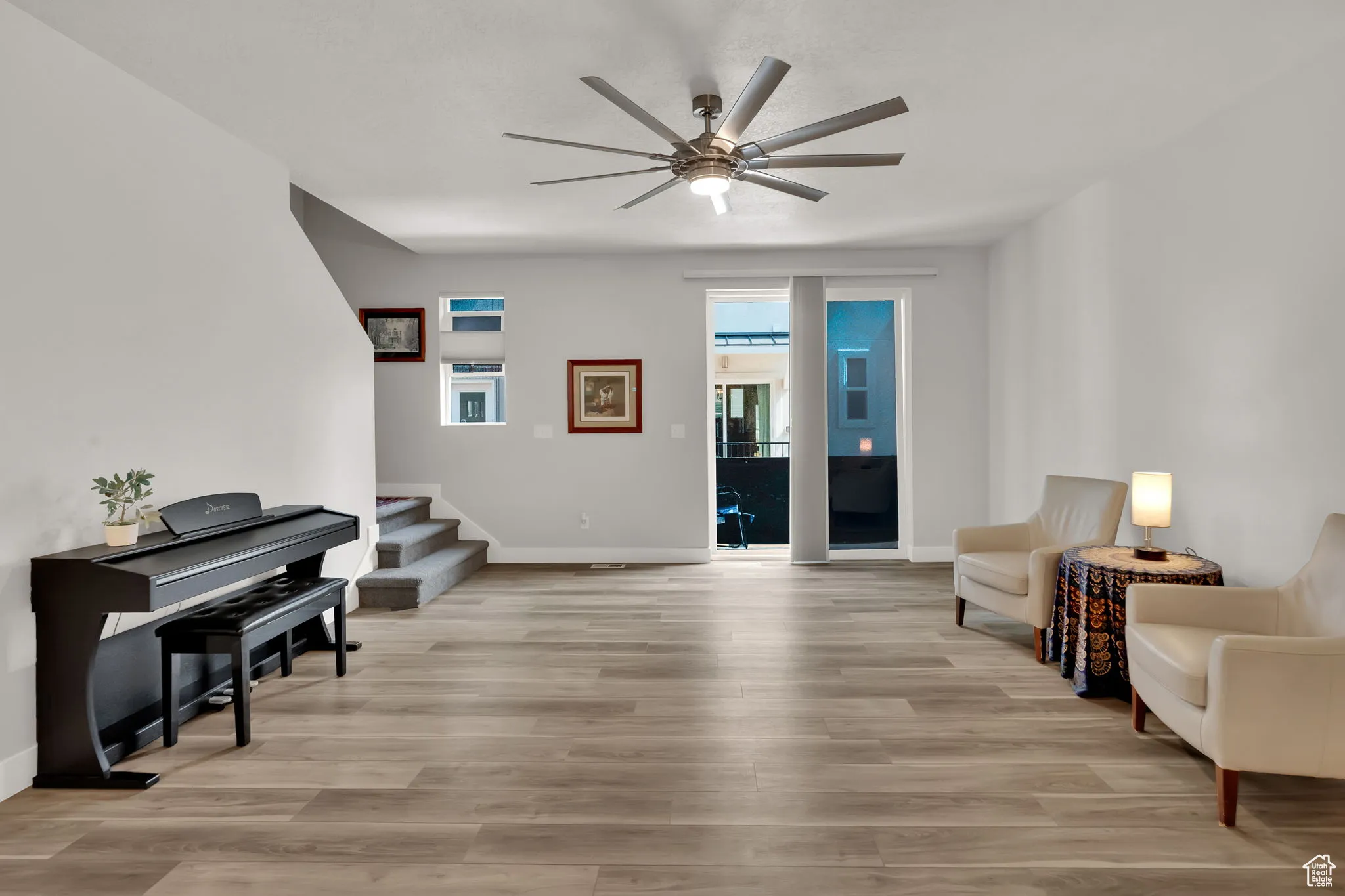 Living area featuring light wood-style LVP floors, stairway, large upgraded ceiling fan and balcony.
