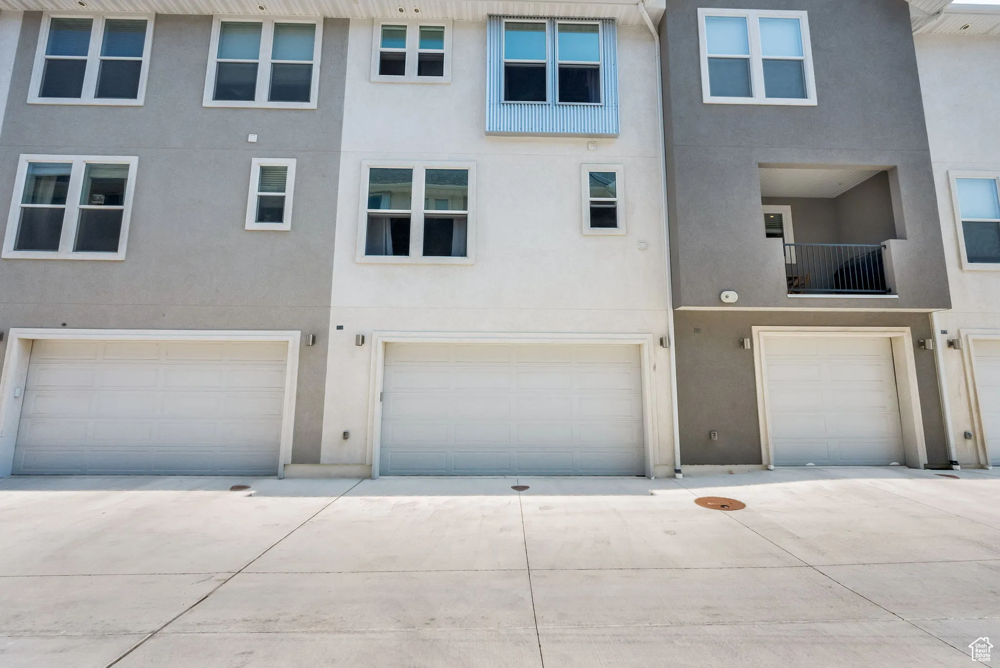 Back of house featuring a balcony, stucco siding, an attached garage, and driveway