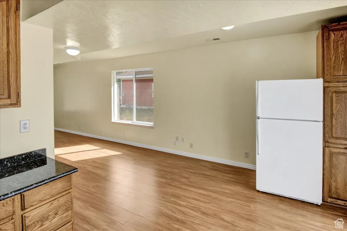 Kitchen with brown cabinets, freestanding refrigerator, light wood finished floors, and dark stone countertops