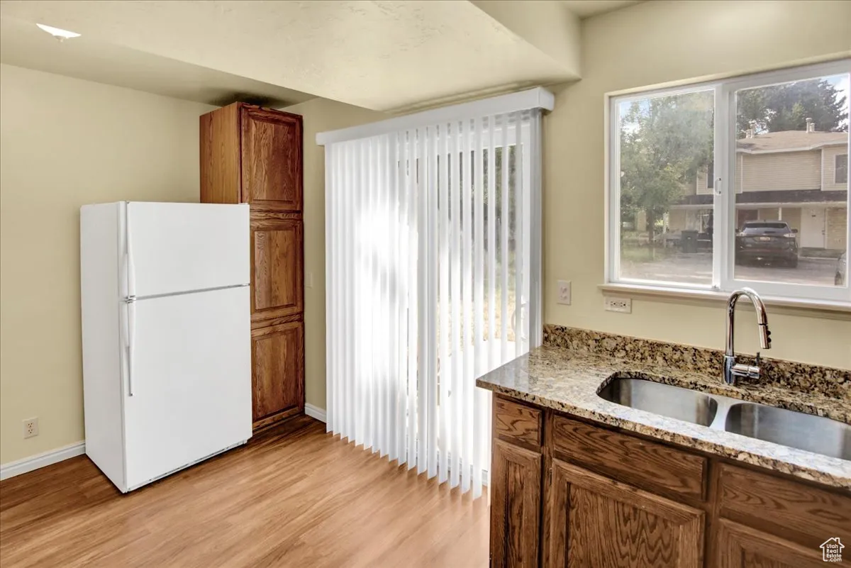 Kitchen with freestanding refrigerator, brown cabinetry, light stone counters, and light wood-type flooring