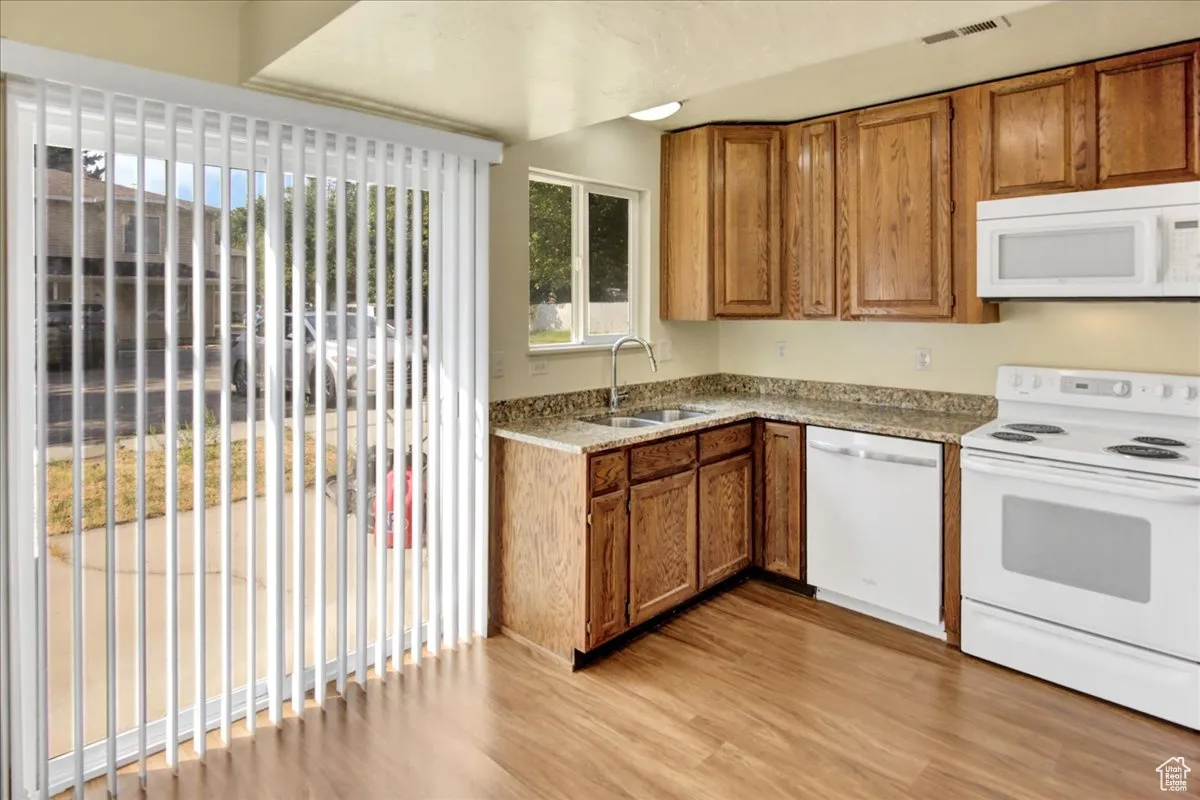 Kitchen featuring white appliances, brown cabinetry, light wood-type flooring, and light stone counters