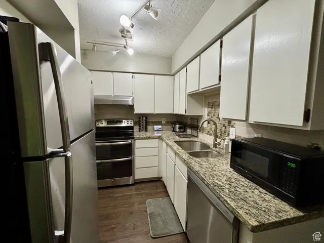 Kitchen featuring stainless steel appliances, light stone countertops, a textured ceiling, white cabinets, and backsplash