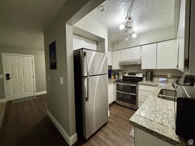 Kitchen featuring stainless steel appliances, light stone counters, white cabinetry, dark wood-style flooring, and a textured ceiling