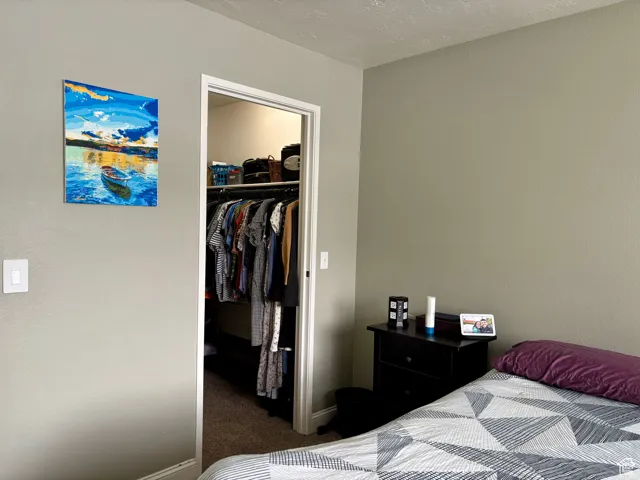 Bedroom featuring dark carpet, a walk in closet, and a textured ceiling