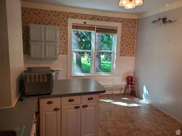 Kitchen featuring a peninsula, wallpapered walls, a wainscoted wall, dark countertops, and tile walls