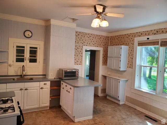 Kitchen featuring wallpapered walls, white cabinets, a wainscoted wall, white range with gas stovetop, and crown molding