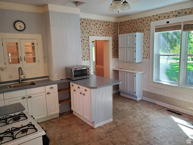 Kitchen featuring white cabinetry, white gas stove, wainscoting, wallpapered walls, and ceiling fan