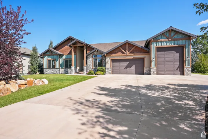 Craftsman inspired home featuring concrete driveway, an attached garage, stone siding, a front yard, and board and batten siding