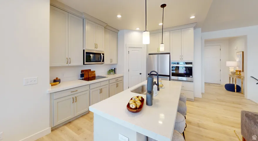 Kitchen featuring light wood-type flooring, stainless steel appliances, recessed lighting, a breakfast bar, and decorative light fixtures